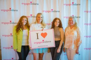 4 women holding a banner of "Engaged Indiana Logo"